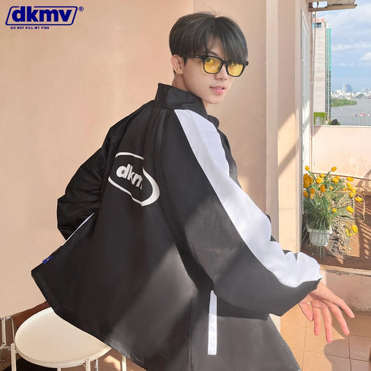 Person wearing a black and white jacket with dkmv logo indoors.
