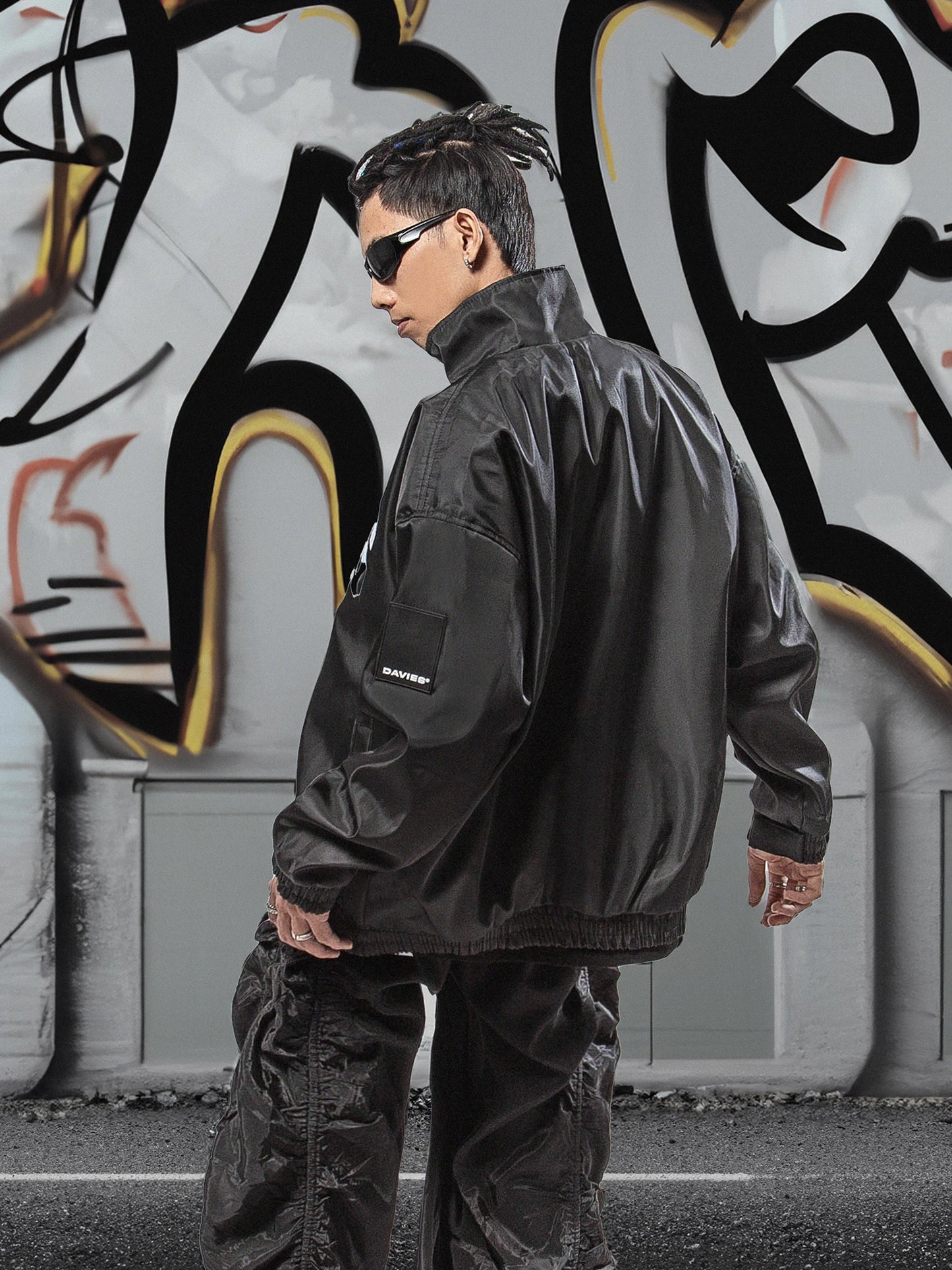 Person wearing a black jacket and sunglasses in front of a graffiti wall