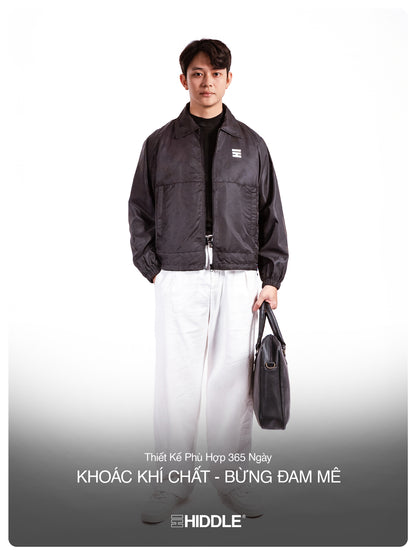 Man wearing a black jacket holding a bag on a white background with Hiddle branding.