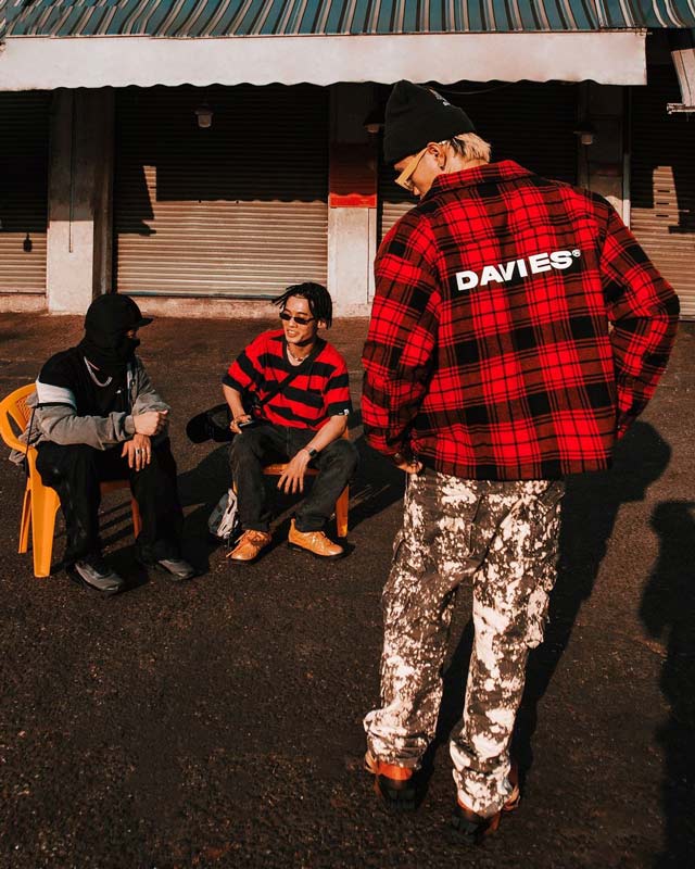 Three people sitting on a bench with one person wearing a red plaid jacket with 'DAVIES' branding.