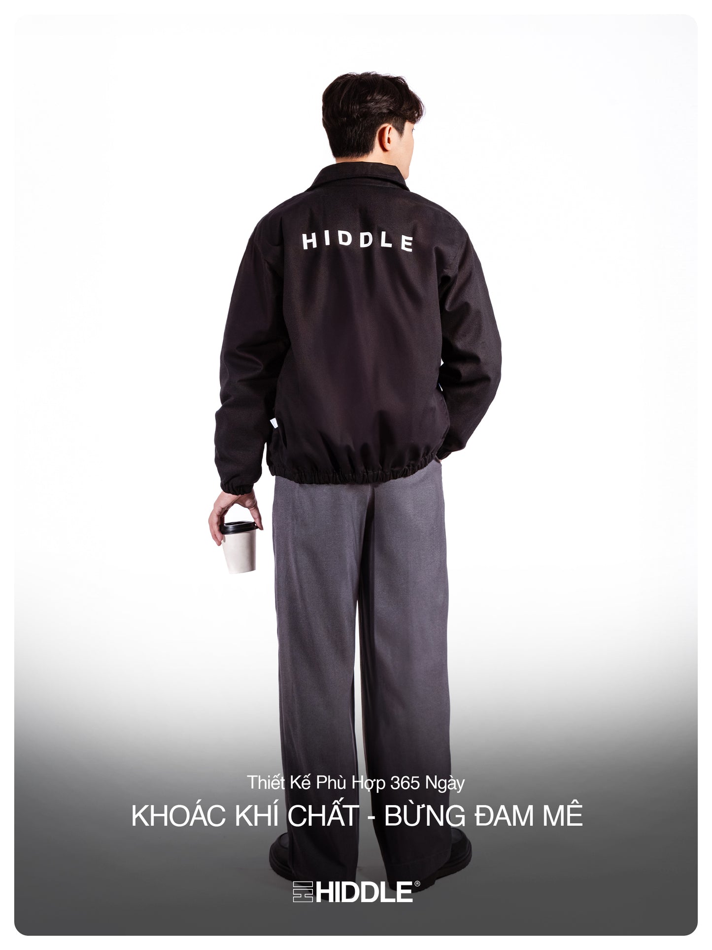 Person wearing a black jacket with 'Hiddle' branding, holding a white cup.