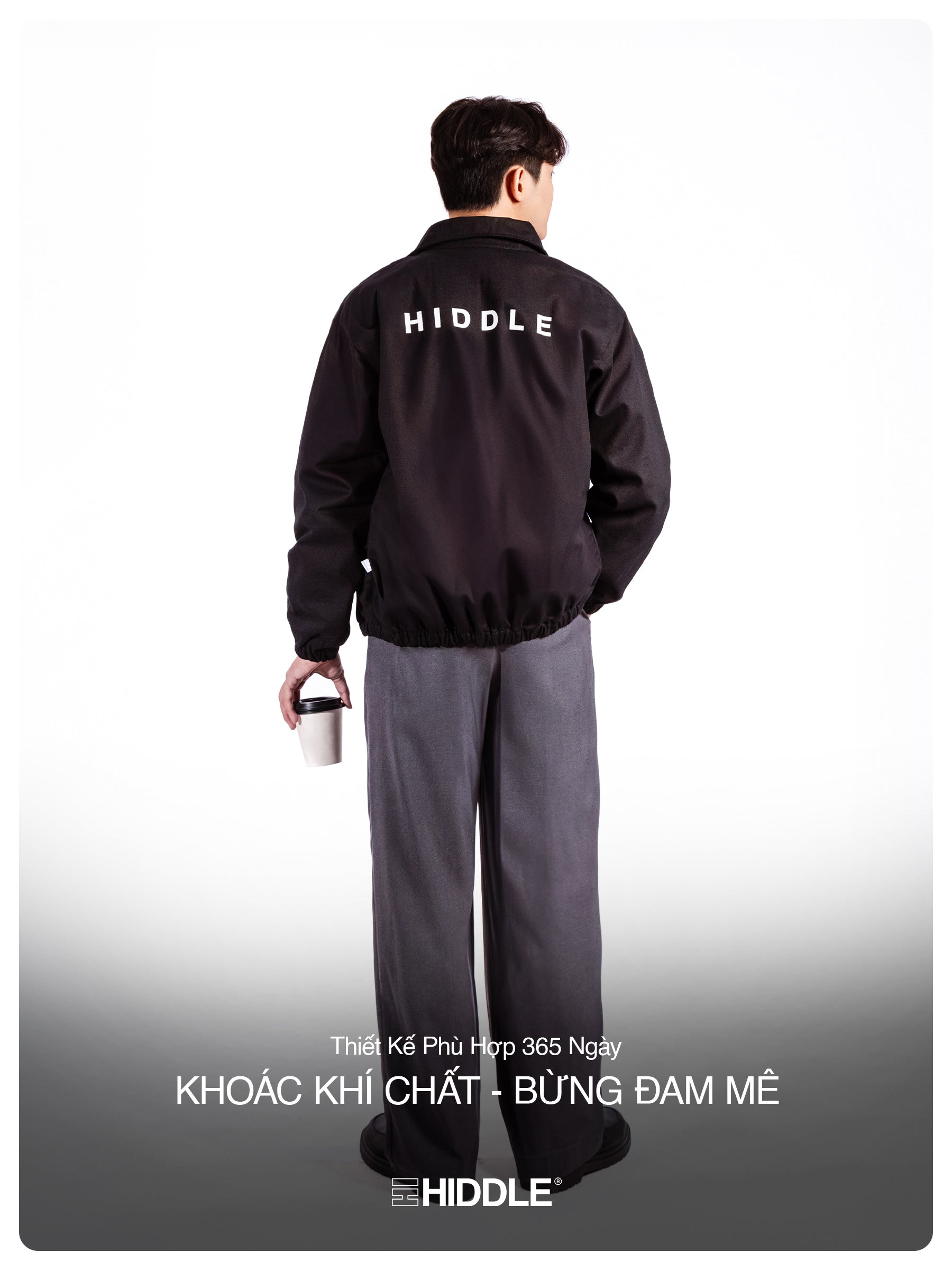 Person wearing a black jacket with 'Hiddle' branding, holding a white cup.