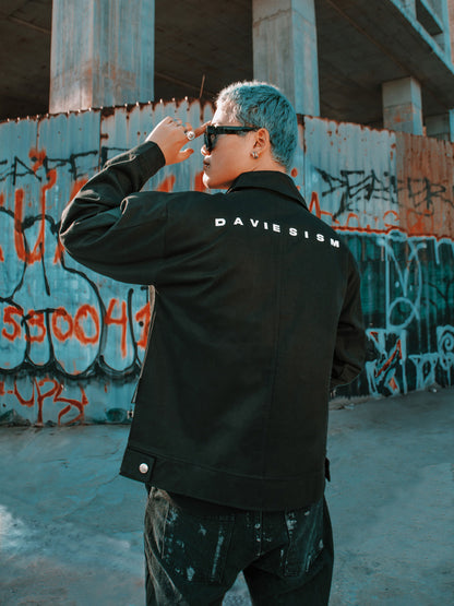 Person wearing a black jacket with 'DAVIESISM' branding in an urban setting with graffiti.