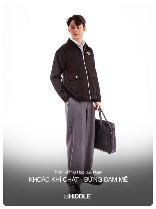 Man holding a briefcase wearing a black jacket and gray pants on a white background with Hiddle branding.