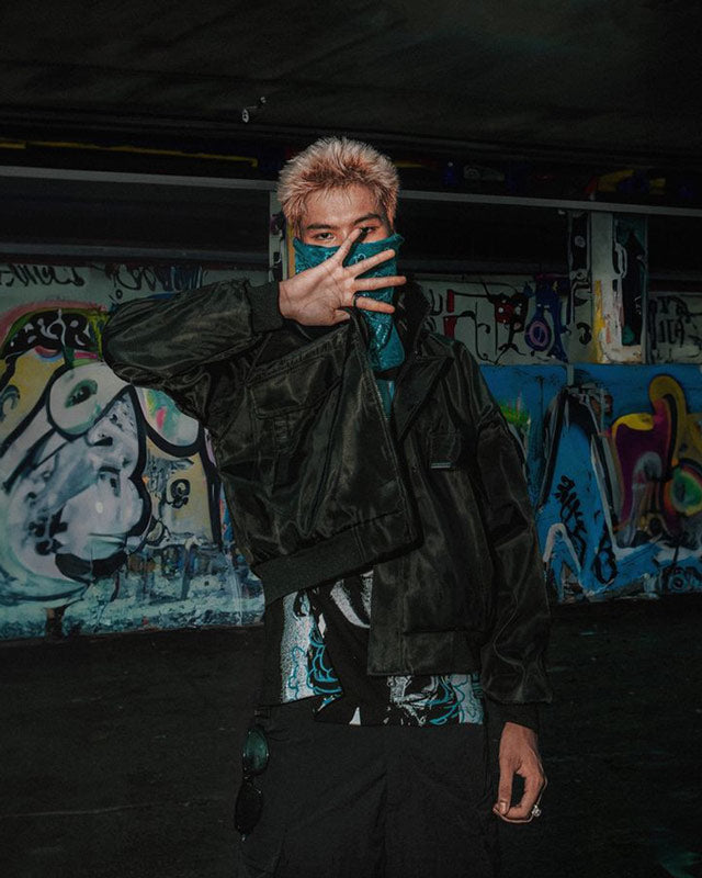 Person wearing a black jacket in front of a graffiti-covered wall