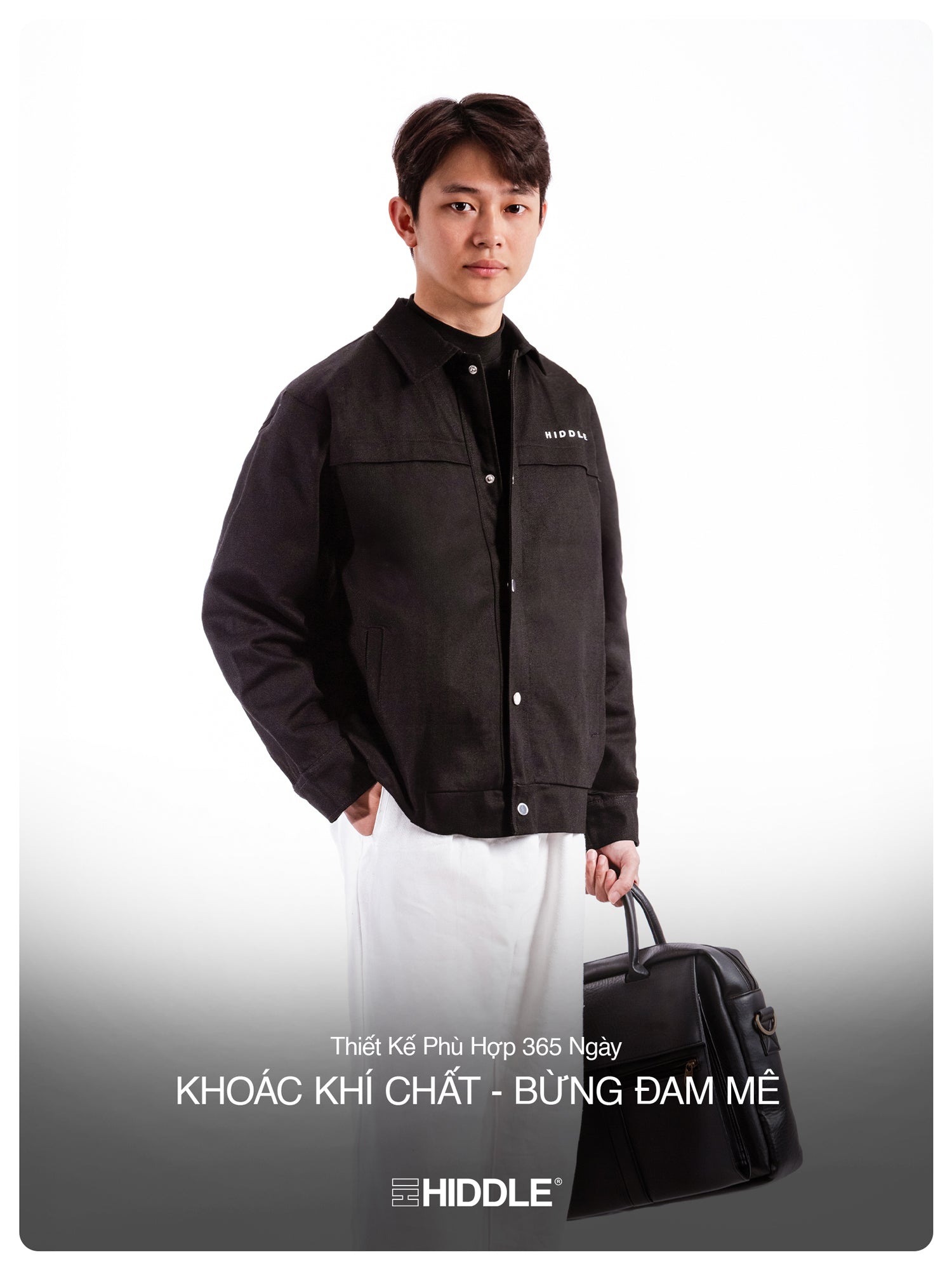 Man wearing a black jacket with a visible brand logo, holding a black bag on a white background.