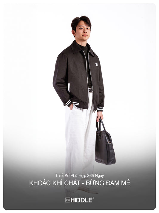 Man wearing a black jacket holding a bag with Hiddle branding on a white background