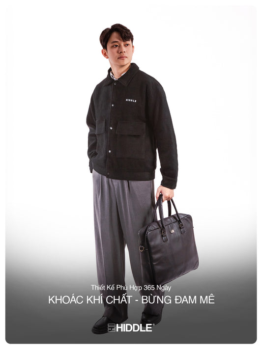Man holding a black briefcase wearing a black jacket with 'Hiddle' branding on a white background.