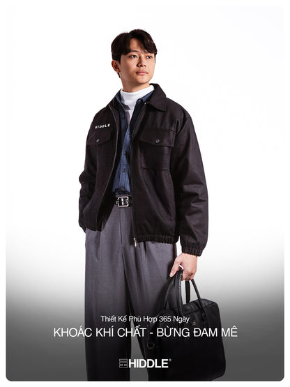 Man wearing a black jacket with 'Hiddle' branding, holding a black bag on a white background.