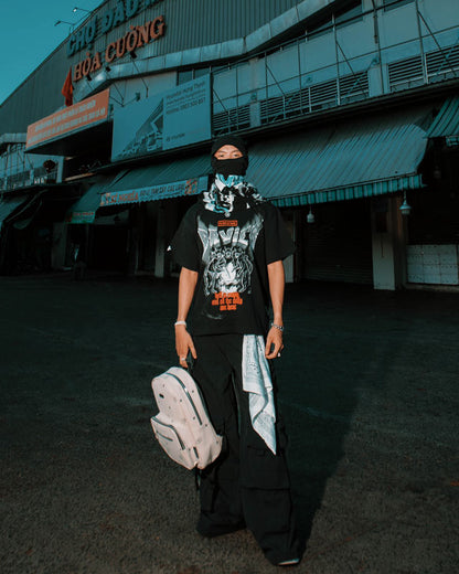 Person wearing a black outfit with a graphic design, holding a white backpack, in front of a building with signage.