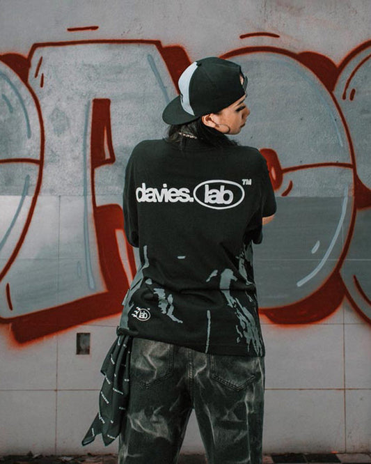 Person wearing a black t-shirt with 'davies lab' branding in front of a graffiti wall.