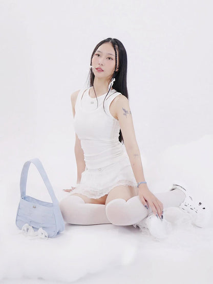 Woman in a white dress sitting on a white surface with a blue bag next to her.