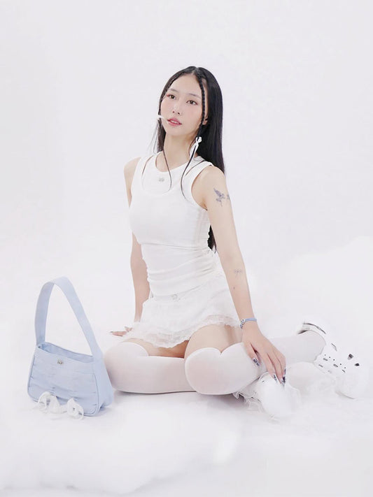 Woman in a white dress sitting on a white surface with a blue bag next to her.