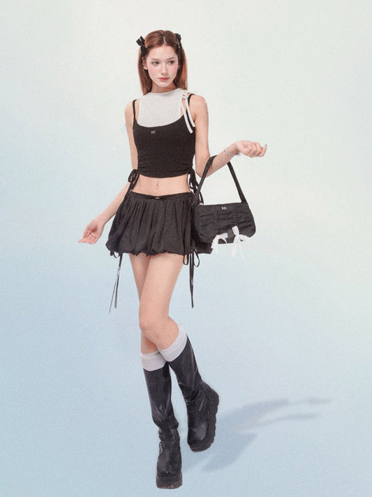 Woman in black outfit with skirt and boots holding a handbag on a light blue background