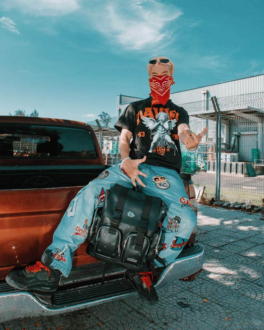 Person sitting on a car with a colorful outfit and bandana, standing against a blue sky.