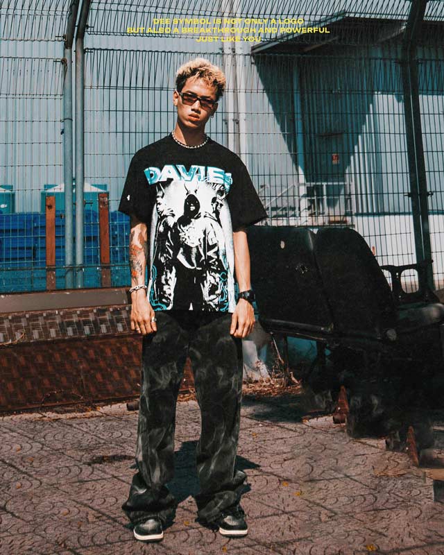 Person wearing a black t-shirt with a graphic design and camouflage pants standing in an urban setting.