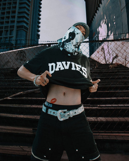 Person wearing a black t-shirt with 'DAVIES' text, black pants, and a face mask in an urban setting.