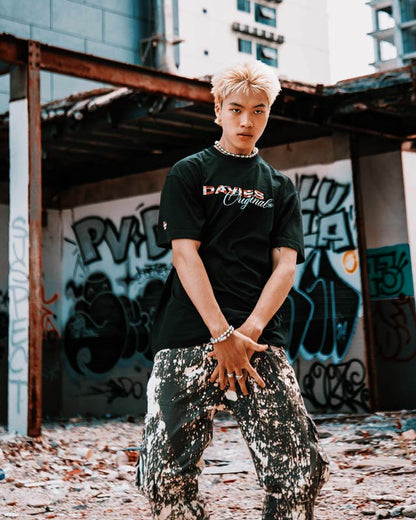 Person wearing a black t-shirt with visible branding in an urban setting with graffiti.