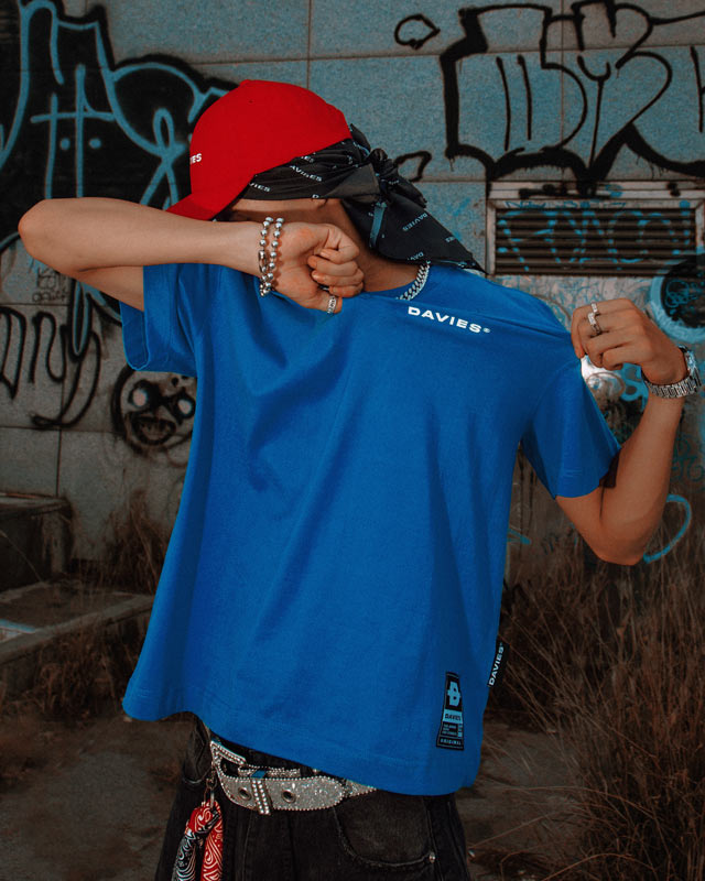 Person wearing a blue t-shirt with 'DAVIES' branding in front of a graffiti-covered wall.