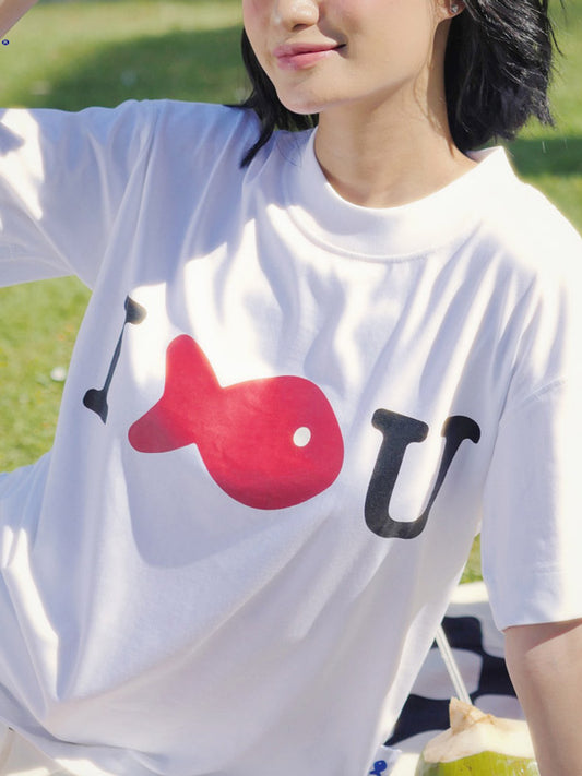 Person wearing a white t-shirt with a red and black graphic design outdoors.