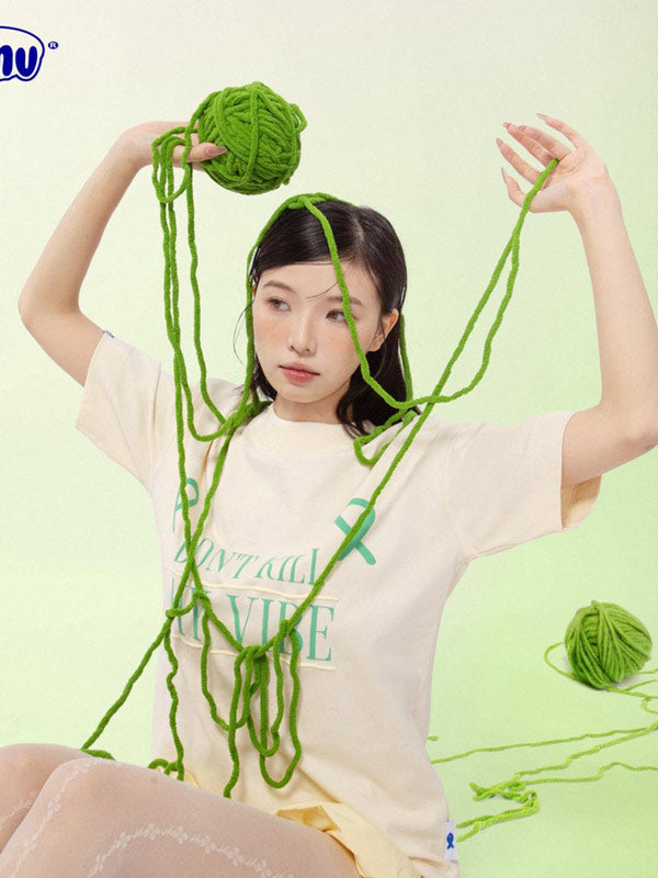 Person with green yarn draped over their head and shoulders on a light green background