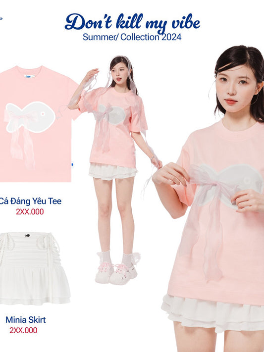 Woman wearing a pink outfit with a bow detail, standing next to a pink t-shirt and white mini skirt.