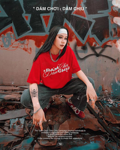 Person wearing a red shirt with text sitting against a graffiti-covered wall.