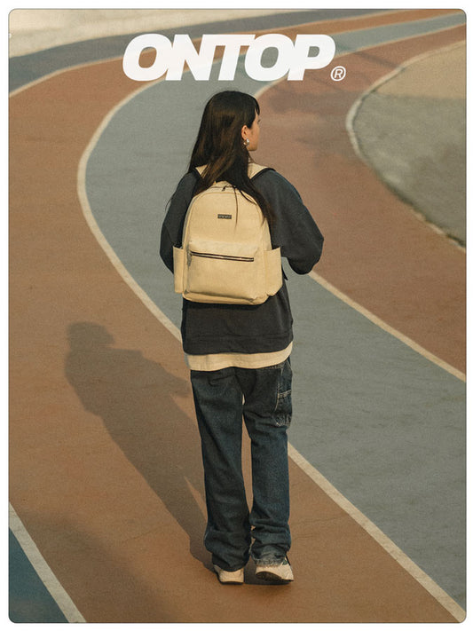 Person with a beige backpack on a track, wearing a black jacket and pants, with 'ONTOP' branding.