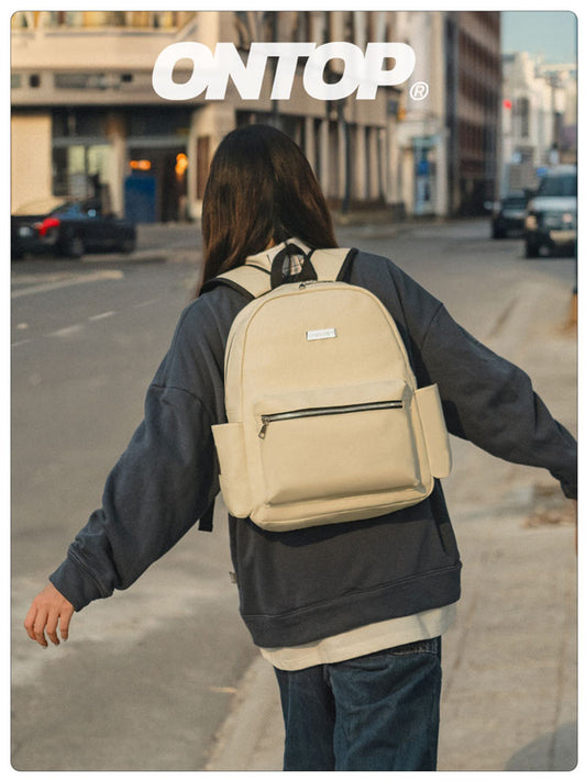 Person wearing a beige backpack with 'ONTOP' branding on a city street.