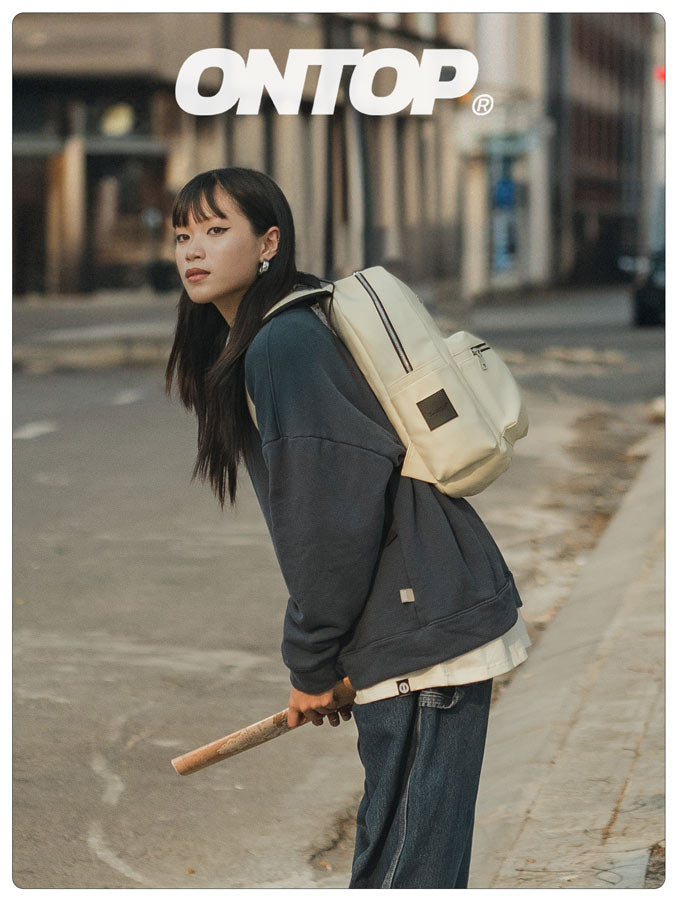 Person wearing a beige backpack and holding a baseball bat on a city street with 'ONTOP' branding.