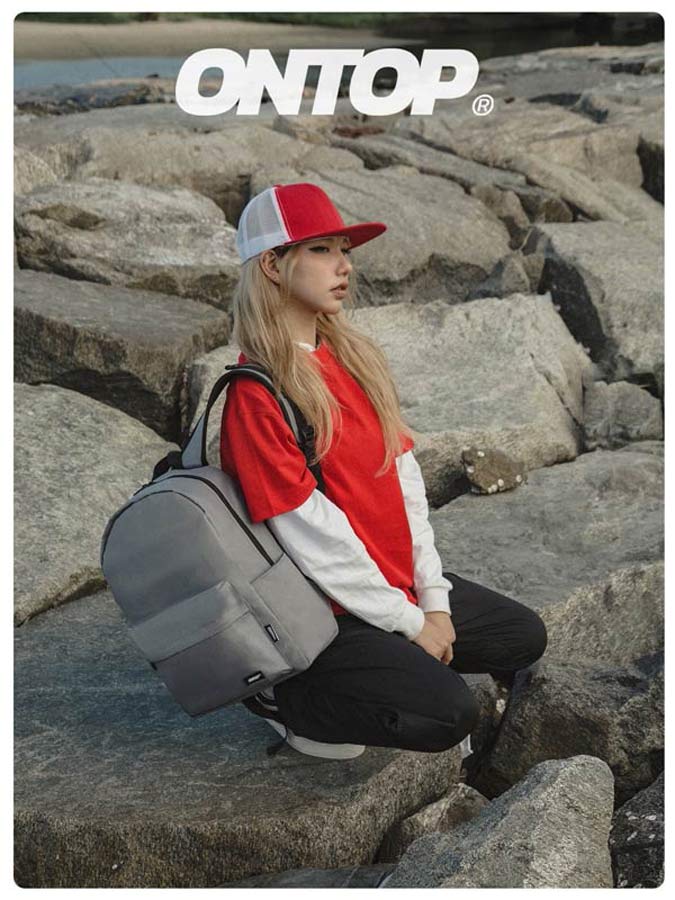Person sitting on rocks with a gray backpack, wearing a red and white cap and red jacket.