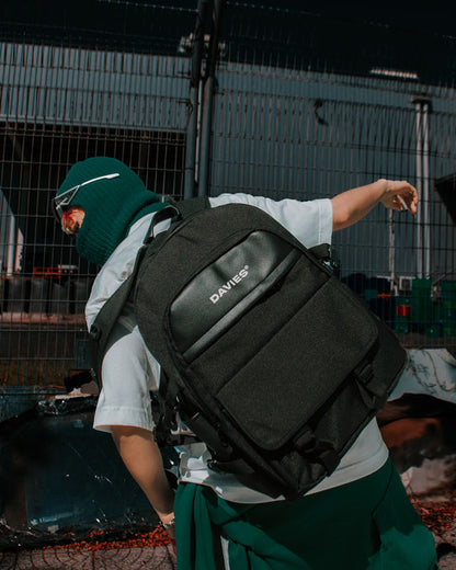 Person wearing a black 'DAVES' backpack in an outdoor setting