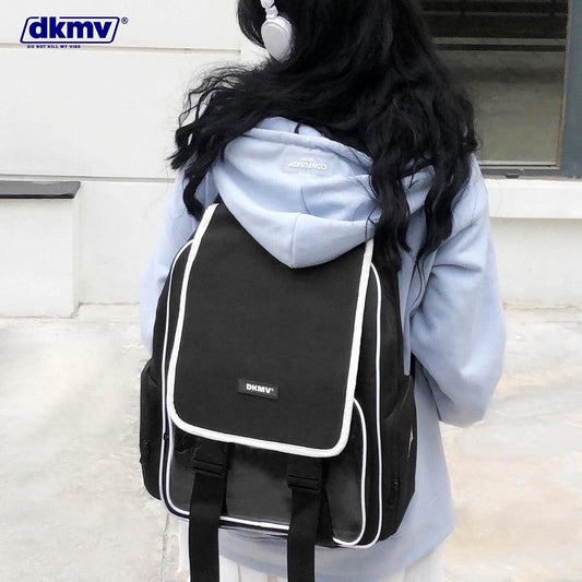 Person wearing a black backpack with 'dkmv' branding, standing against a neutral background.