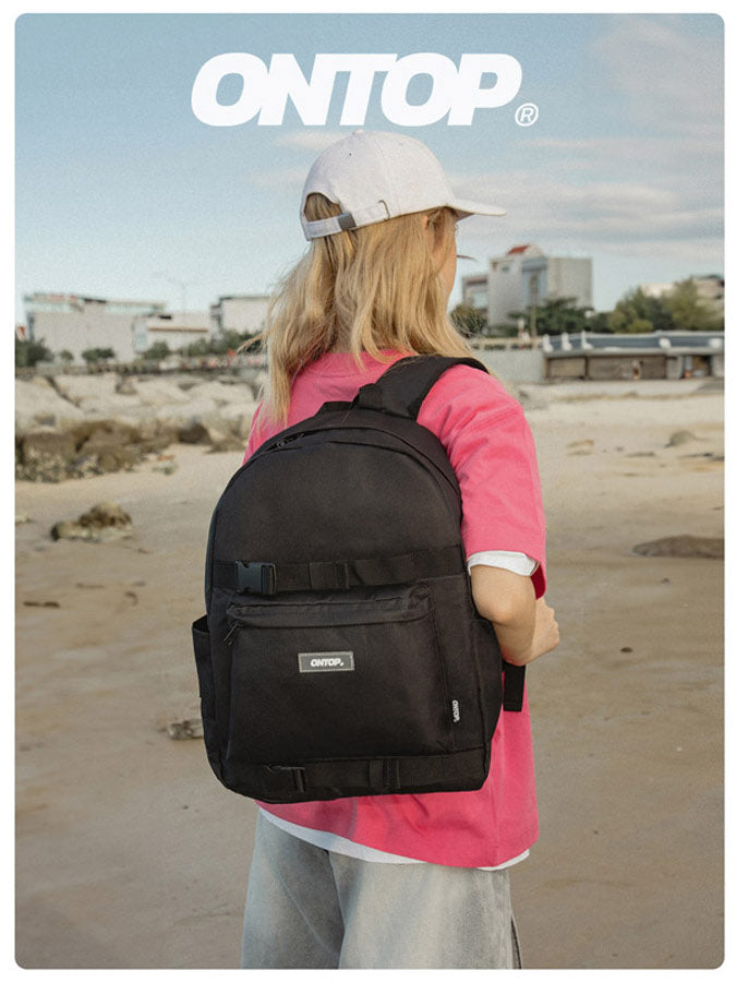 Person wearing a black backpack with 'ONTOP' branding on a beach.