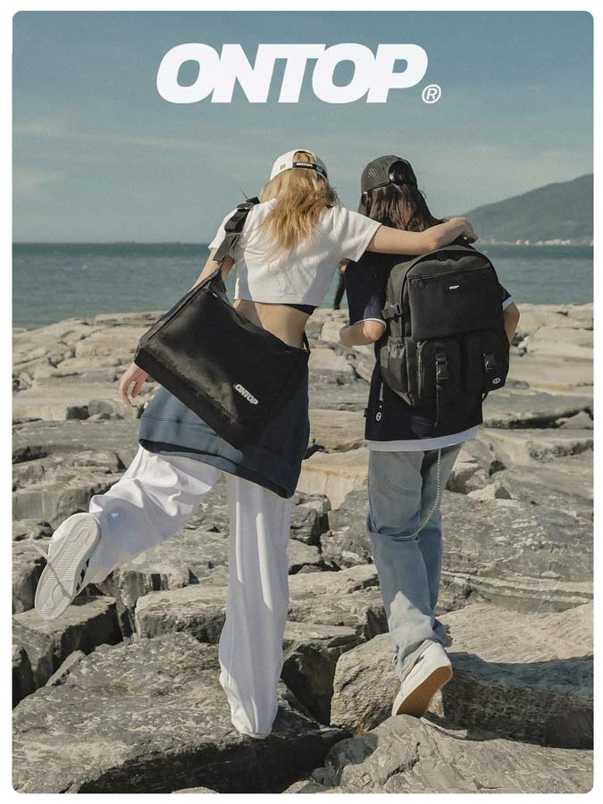 Two people walking on rocks by the sea with 'ONTOP' bags.