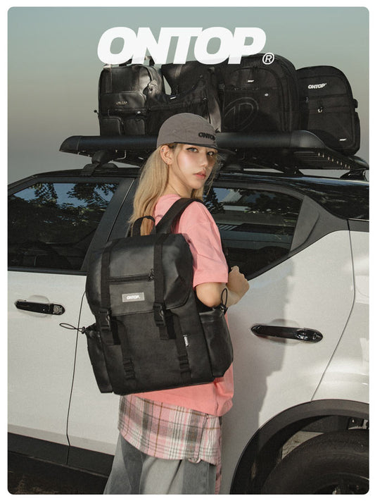 Person holding a black backpack with a car and roof racks in the background, featuring the 'ONTOP' brand.