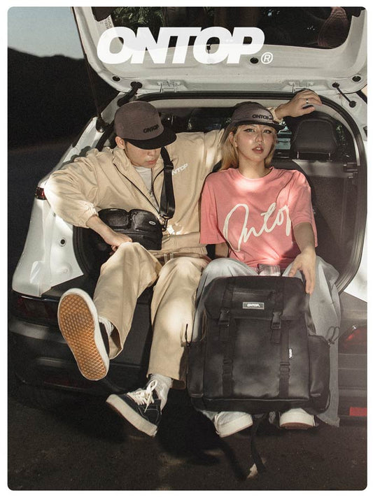 Two people sitting in the back of a car with luggage, wearing 'ONTOP' branded clothing.