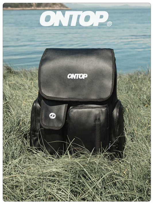 Black backpack with 'ONTOP' branding on grass near a body of water