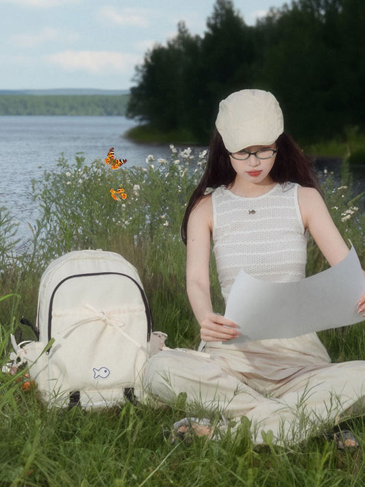 Woman sitting by a lake reading a book with a backpack next to her