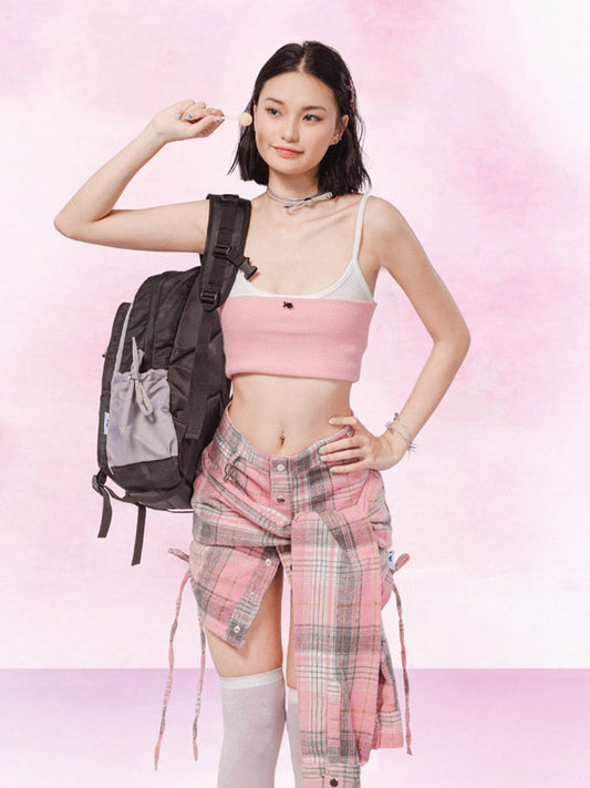Woman in pink sports bra and plaid shorts with a backpack on a pink background