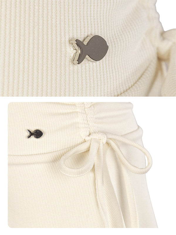 Close-up of a ribbed knit garment with a small fish-shaped button on a white background.