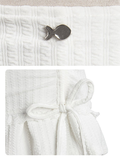 White textured fabric with a small fish-shaped brooch on a beige background