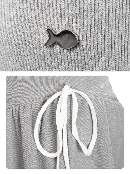 Gray beanie with a small fish-shaped brooch and white drawstrings on a gray background