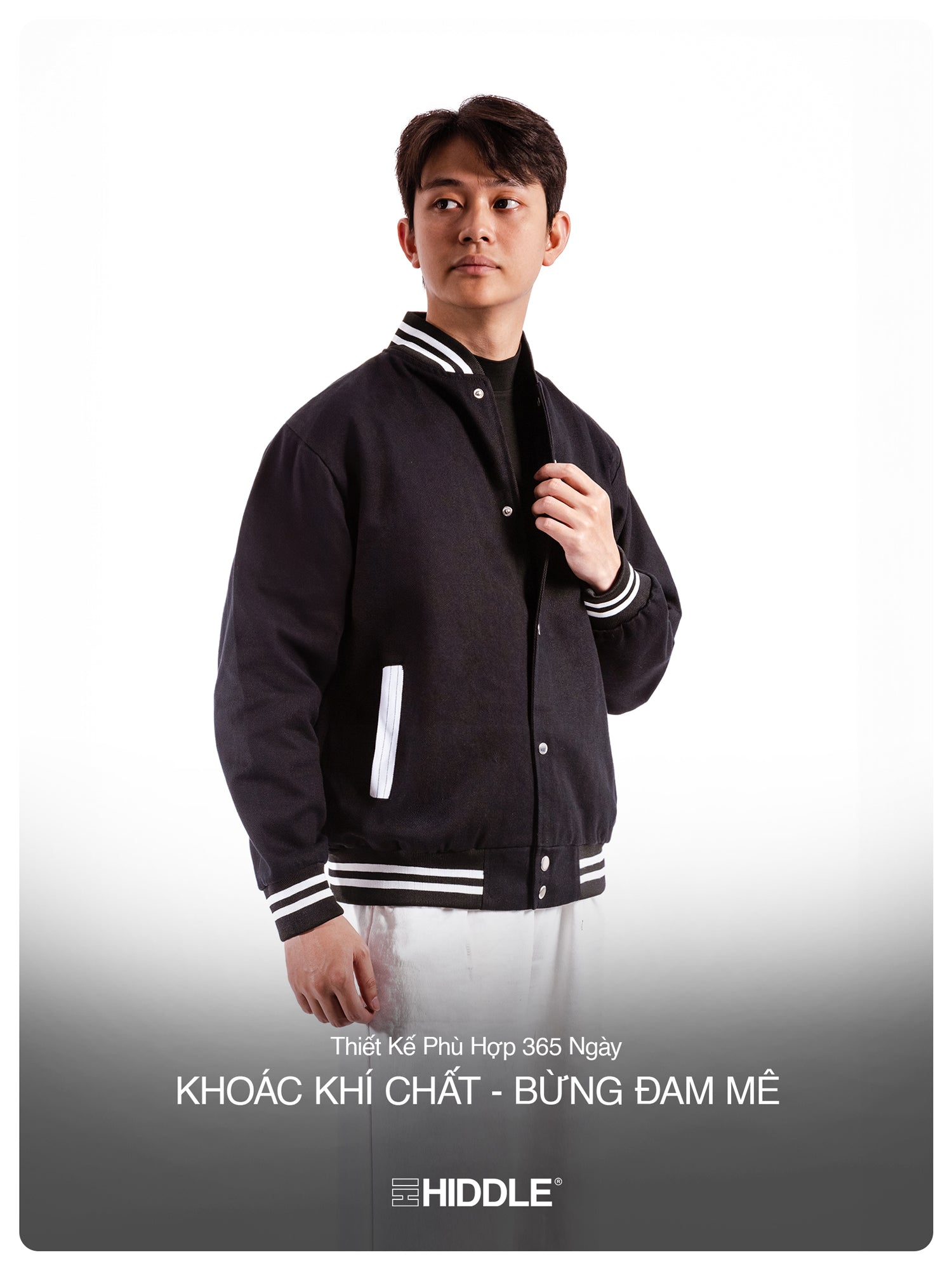 Man wearing a black varsity jacket with white accents, standing against a plain background.