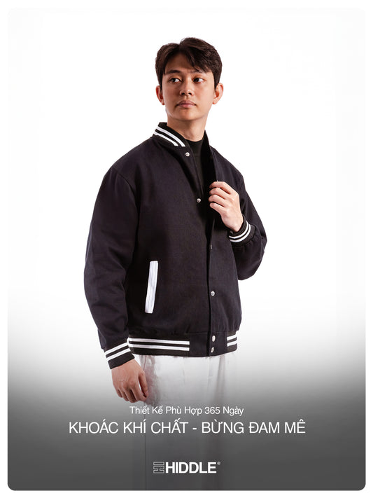 Man wearing a black varsity jacket with white accents, standing against a plain background.