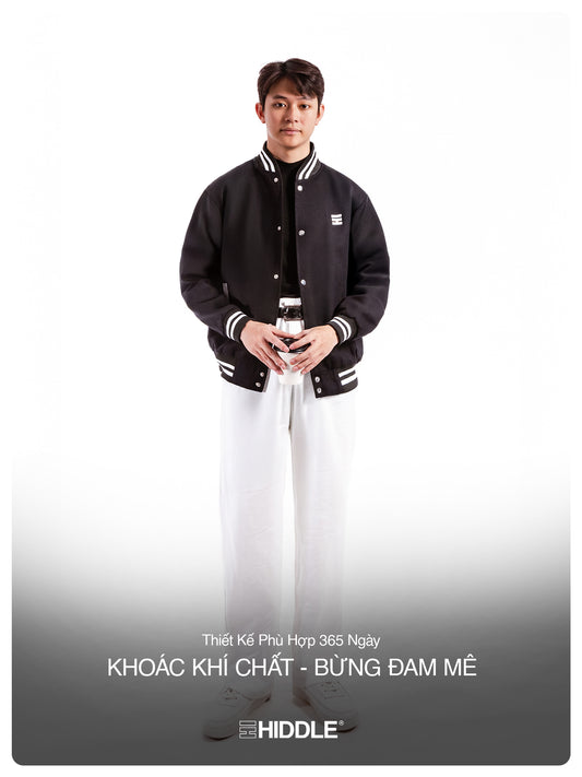 Person wearing a black varsity jacket with white accents on a white background