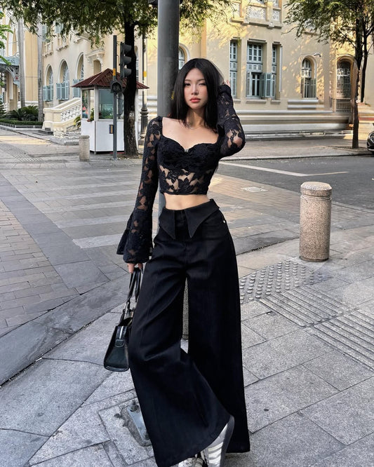 Woman in black lace top and wide-leg pants standing on a city street.
