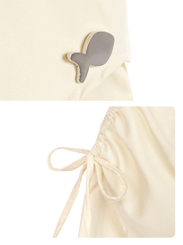 Close-up of a beige dress with a decorative bow and a small gray embellishment on a white background.
