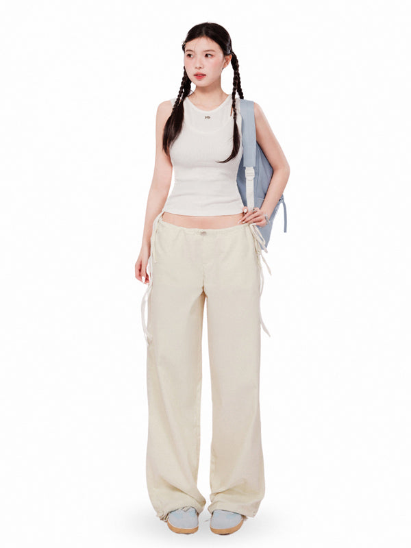 Woman wearing a sleeveless top and beige pants with a backpack on a white background