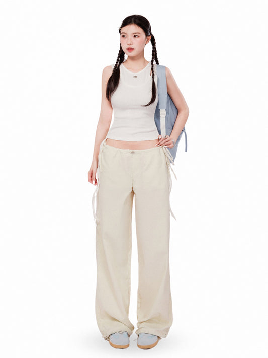 Woman wearing a sleeveless top and beige pants with a backpack on a white background